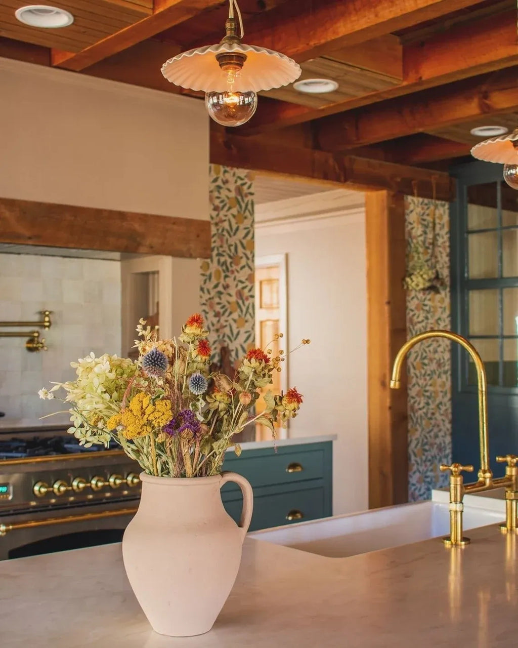 Kitchen with a vase of flowers on the counter, wooden beams, and a sink with gold fixtures.