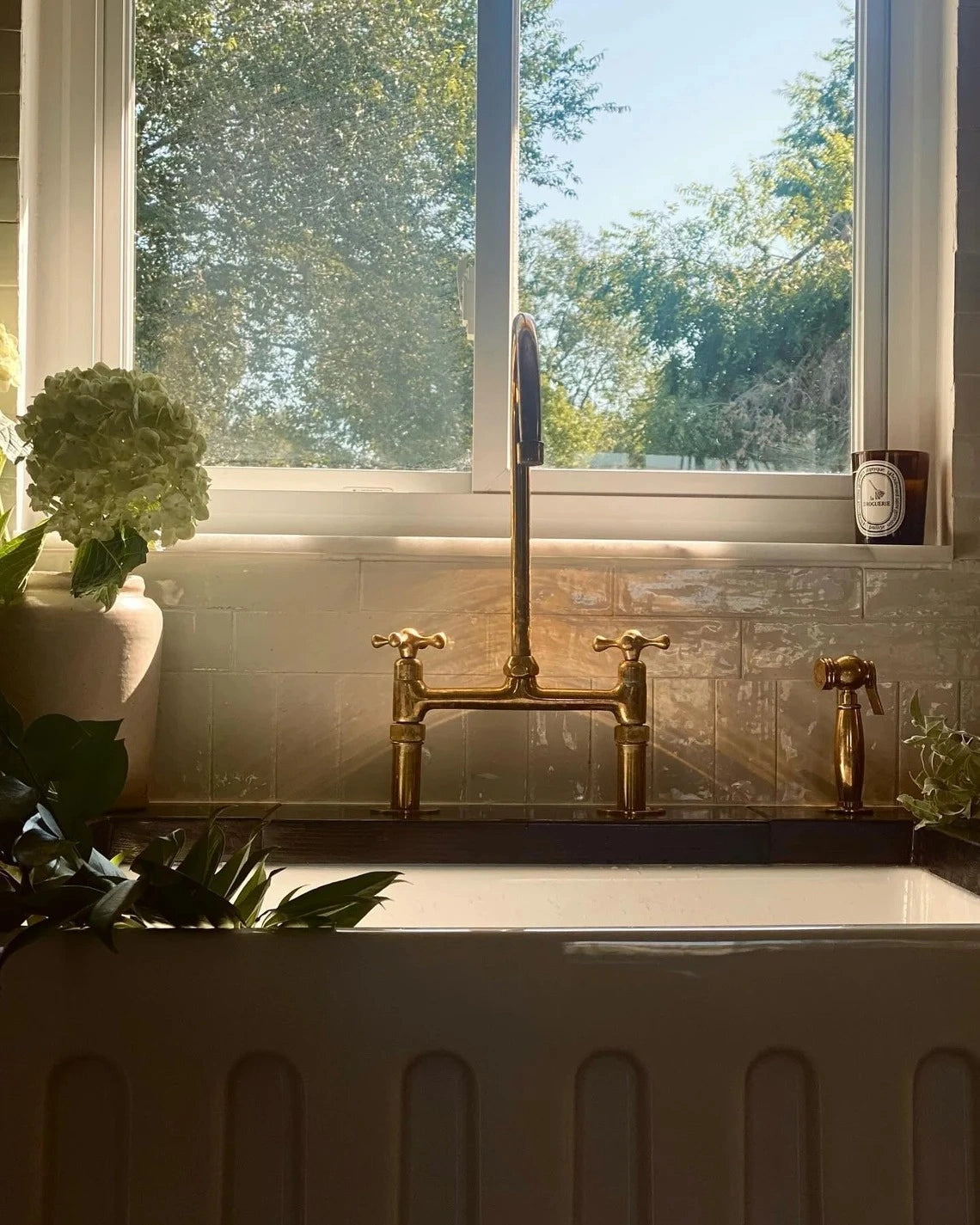 Vintage-style brass kitchen faucet on a white sink with a window in the background