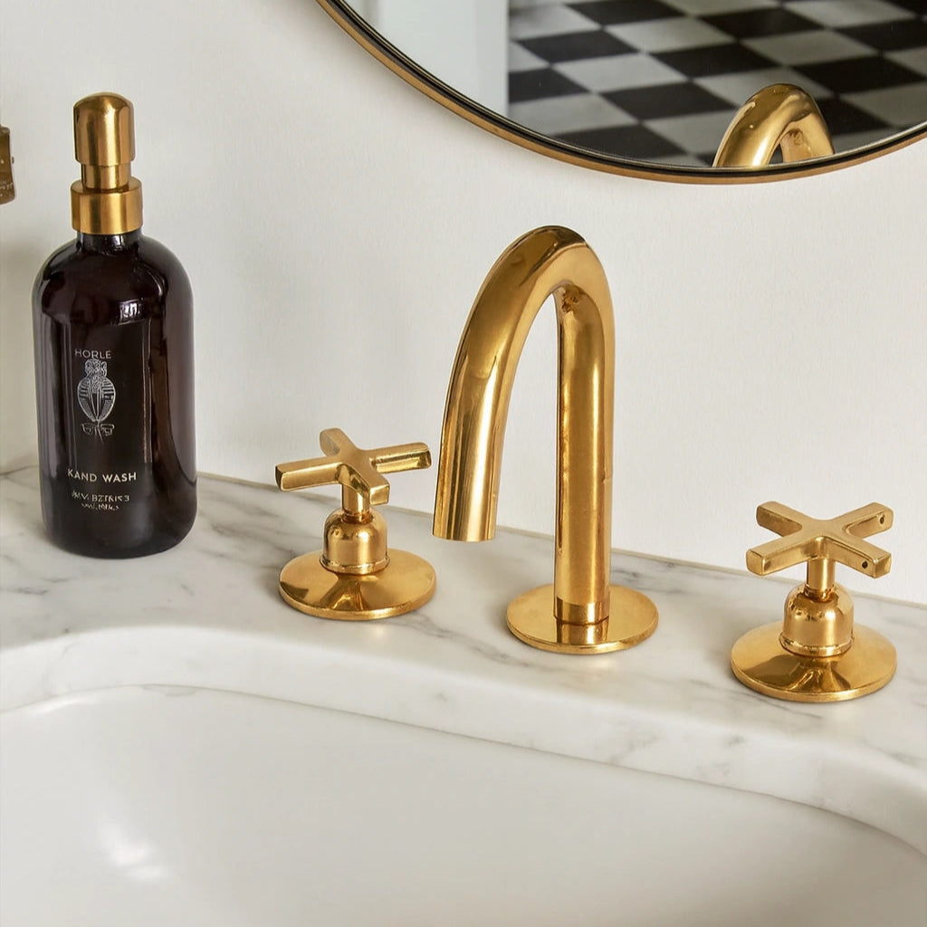 Gold faucet and handles on a marble sink with a bottle of soap next to it.