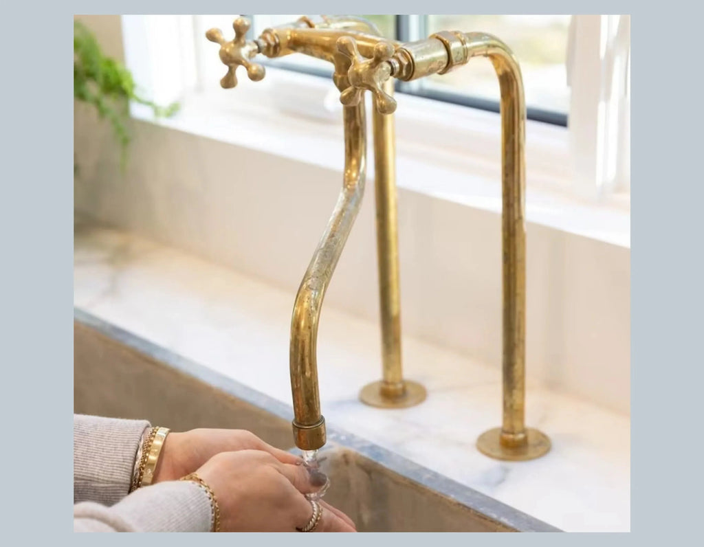 Brass faucet with water flowing into a sink, set against a neutral background.