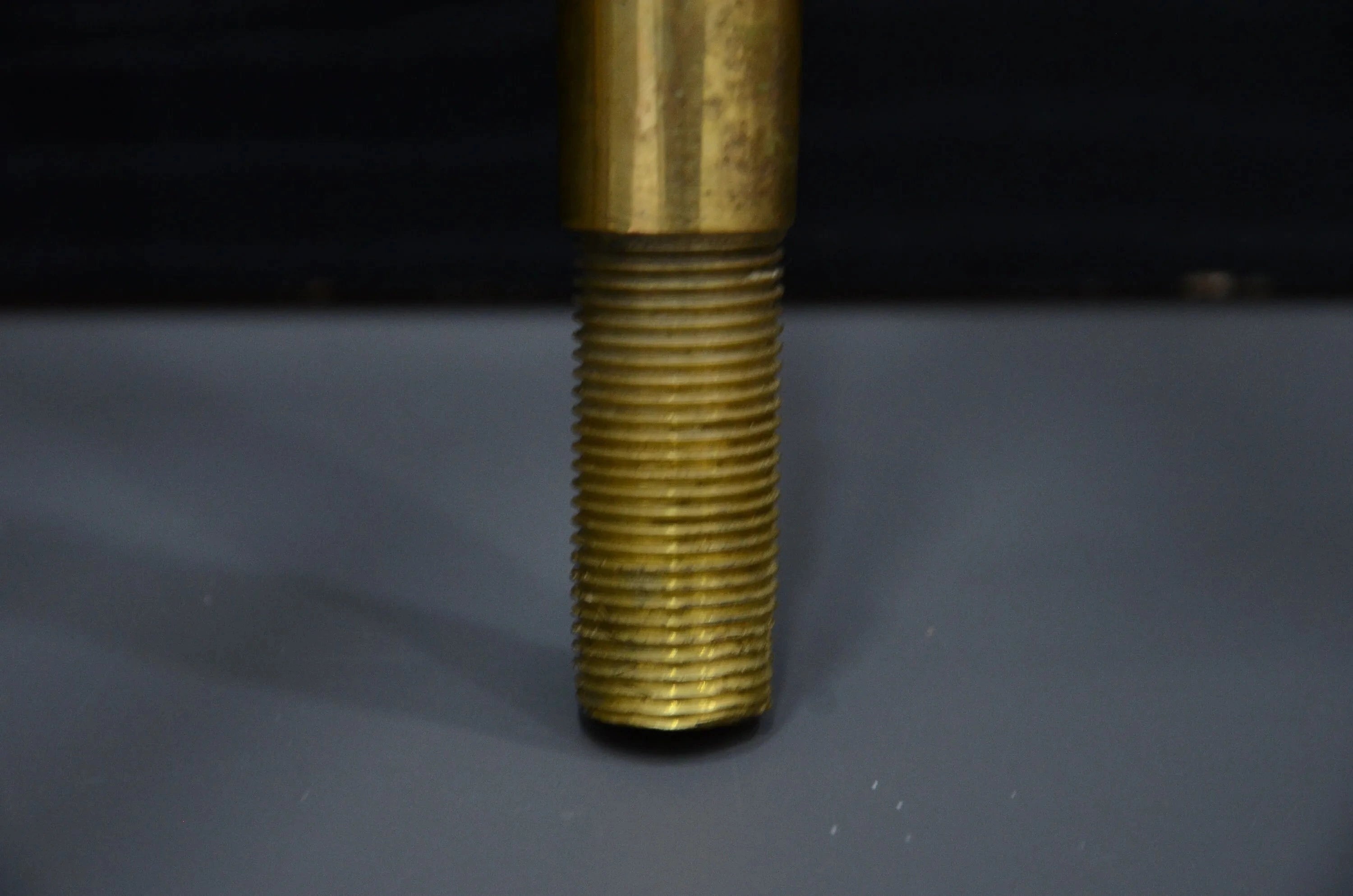 Close-up of a threaded brass rod on a dark background
