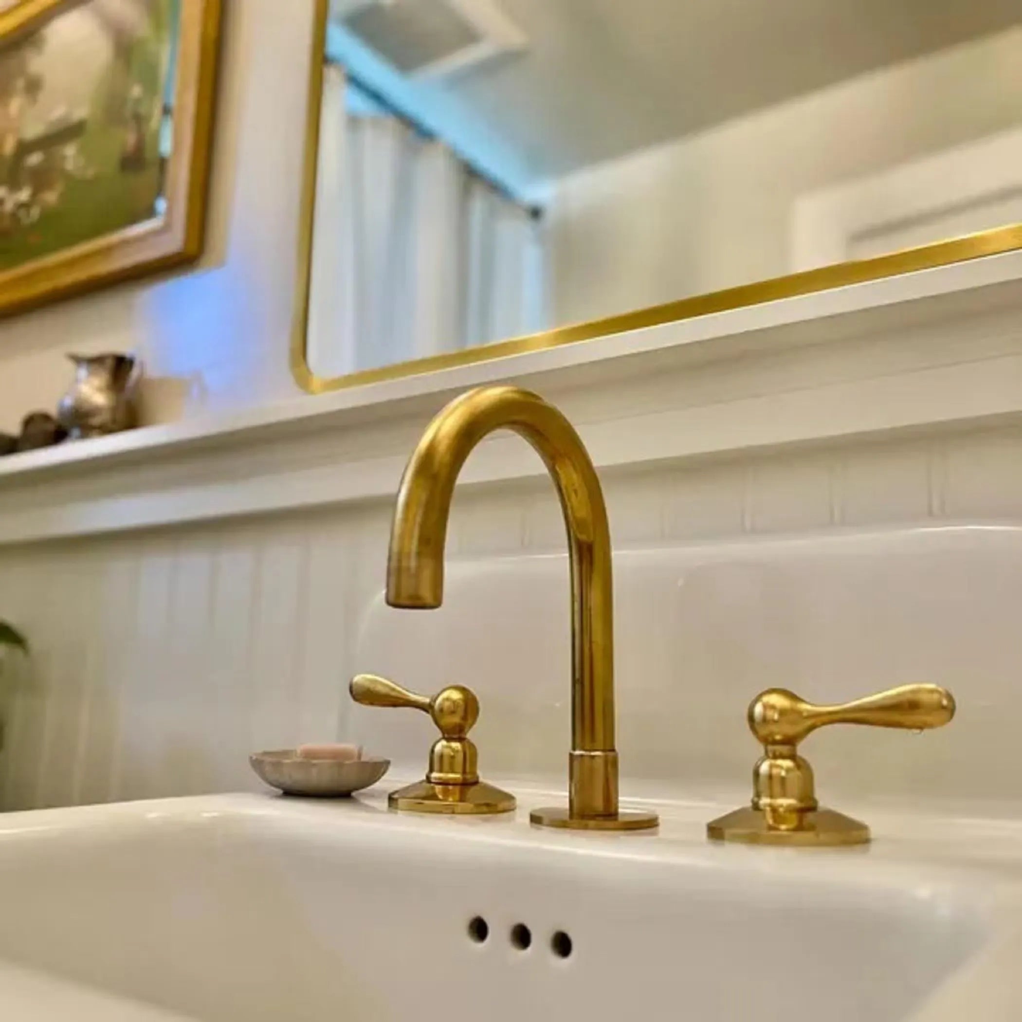 Gold faucet and handles on a white sink with a mirror in the background